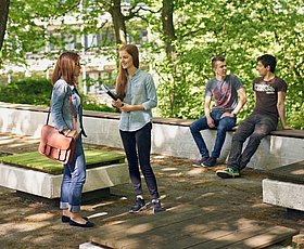 Mehrere Studierende auf dem baumbewachsenen Außengelände am Campus Grifflenberg