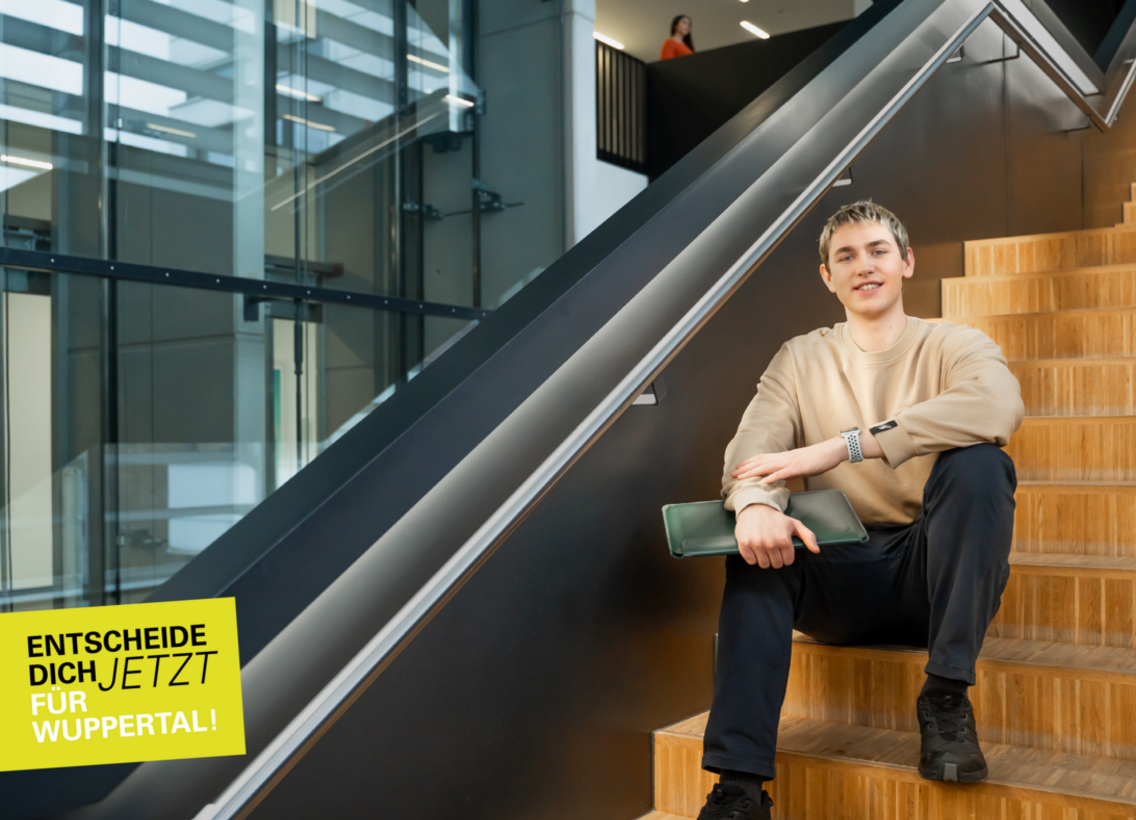 Ein Studierender sitzt auf einer Treppe. Er hält einen Laptop in der Hand.
