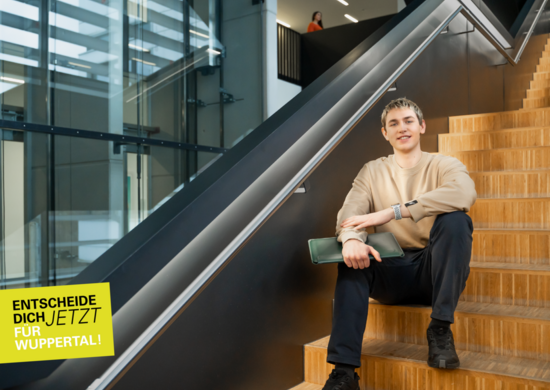 Ein Studierender sitzt auf einer Treppe. Er hält einen Laptop in der Hand.